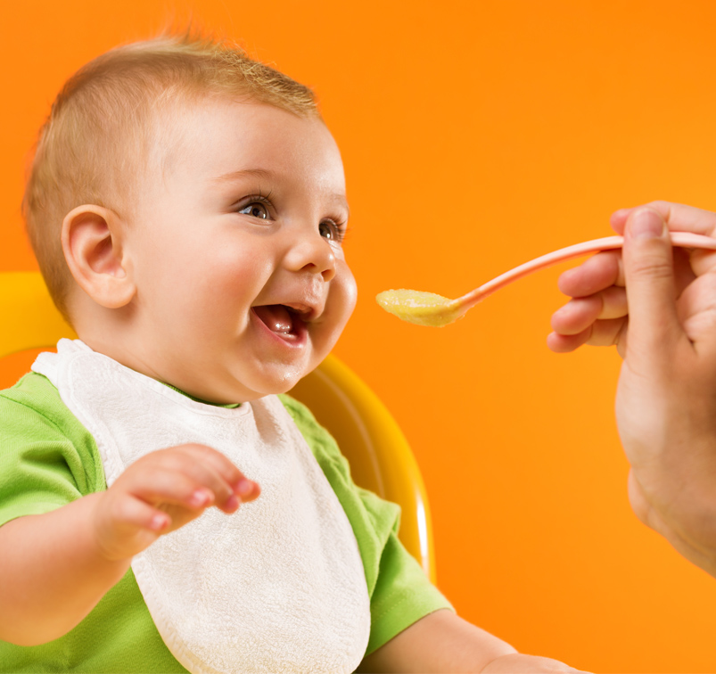 Baby wird mit einem Löffel gefüttert und lacht dabei.