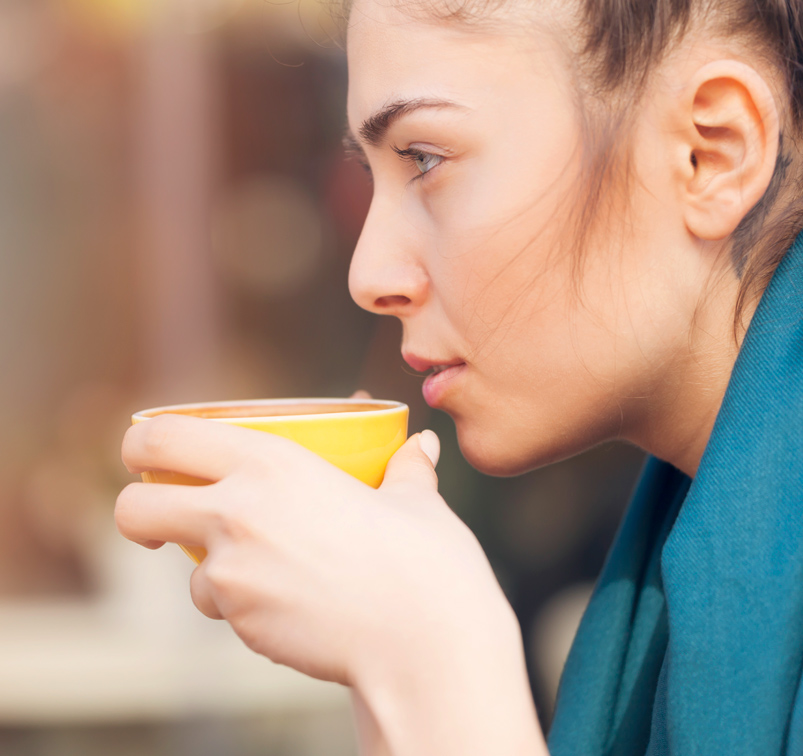 Ruhige, junge Frau trinkt Kaffee aus einer großen Tasse.