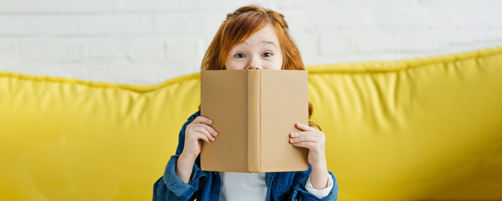 Aufgewecktes Mädchen schaut über Buchrand.